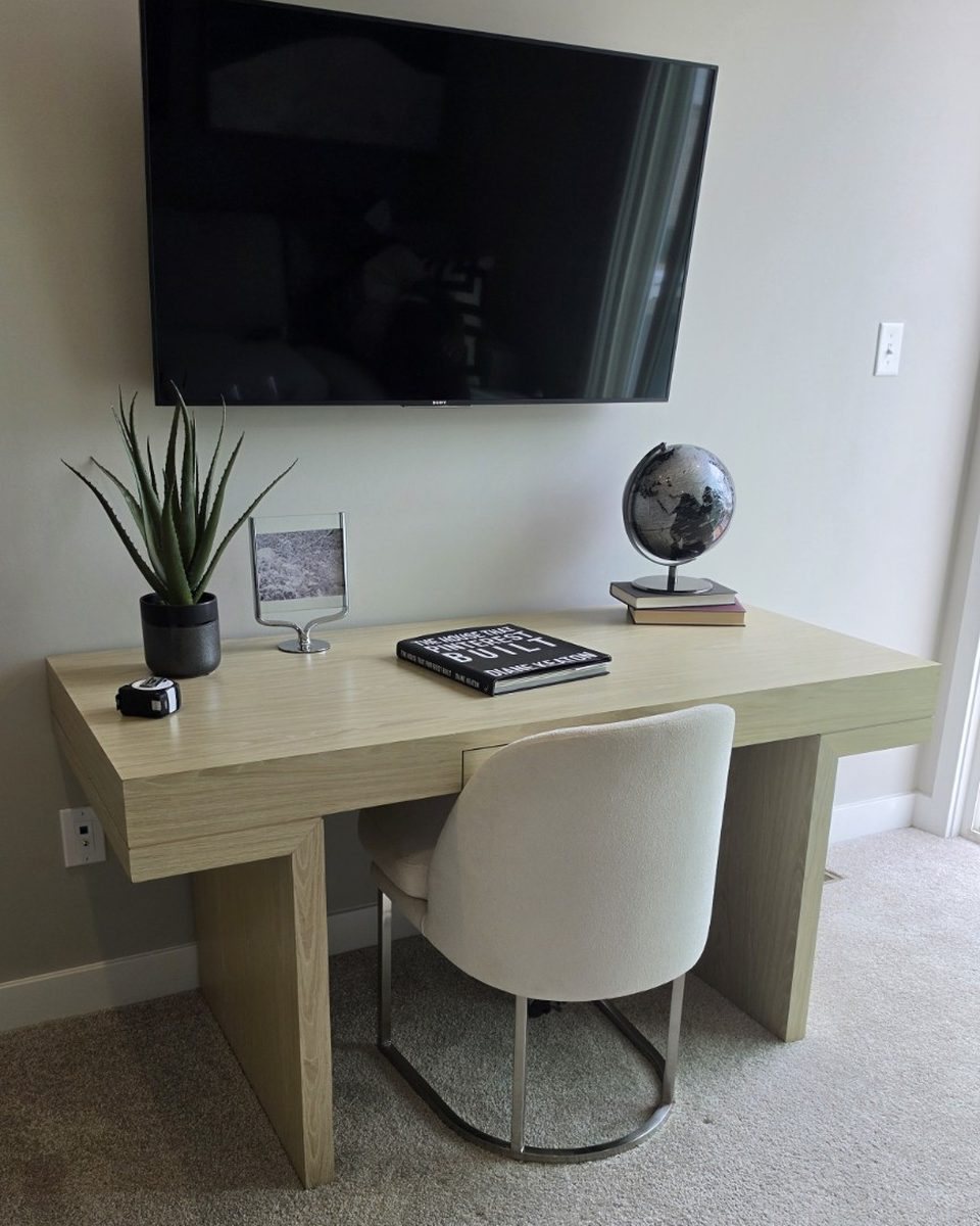 A calm desk nook under a wall-mounted TV with a plant and books